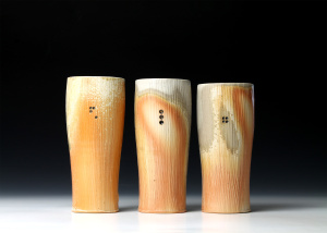 Three tall tumblers with orange-ish glaze which are wood fired.