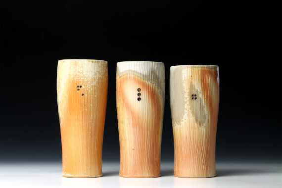 Three tall tumblers with orange-ish glaze which are wood fired.