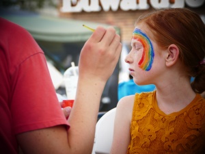 girl with face painting of a rainbow on her cheek