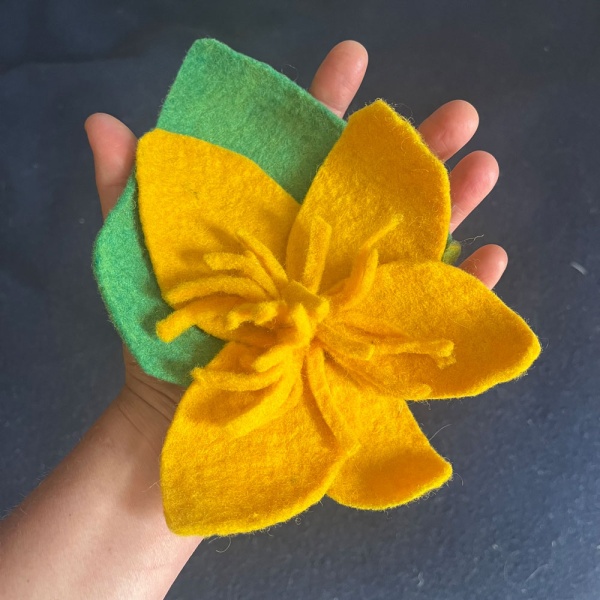hand holding a yellow felted flower with green background leaf