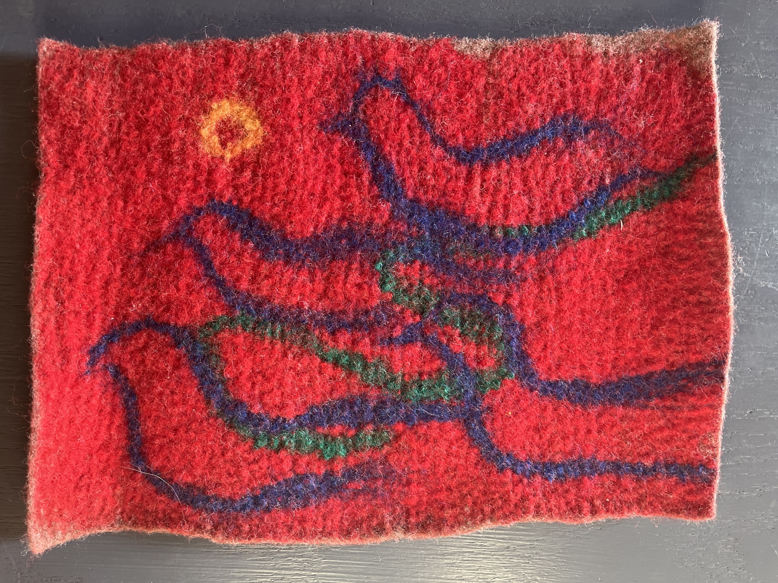 felted red tapestry with blue whispy lines representing bird shapes