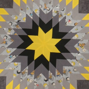 8 point star quilt with yellow in the middle, black, gray and cartoon patterns radiating out in concentric layers